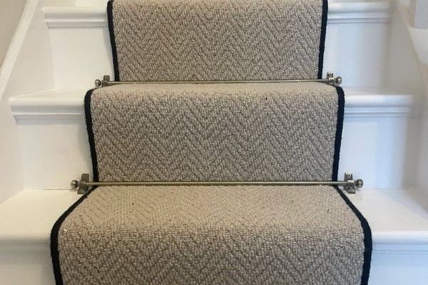 neutral beige herringbone wool carpet stair runner on white wooden staircase with brushed brass stair rods